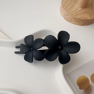 Détail d'une pince à cheveux double fleur noir mat posée sur un plateau en céramique