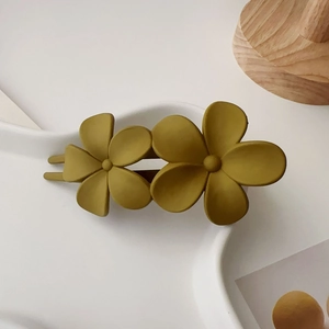 Détail de pinces à cheveux florales vert moutarde mat sur une assiette décorative