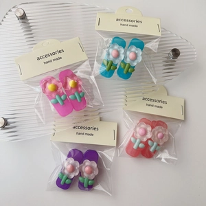 Dettaglio di quattro fermagli per capelli a fiori in resina blu, rosa e viola con confezione