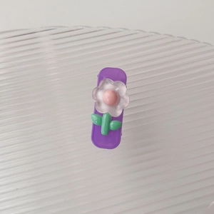 Dettaglio di un fermaglio viola per capelli con petali smerigliati e foglie verdi