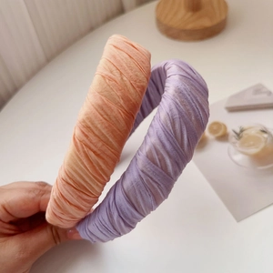 Detail showing hand holding orange and purple pleated silk-texture wide headbands