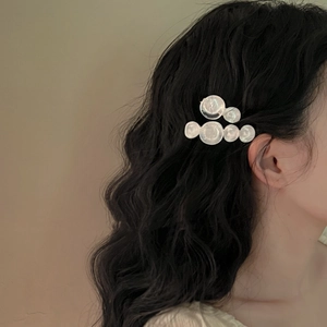 Detailed view of white pearlescent wave circle hair clip on long black hair