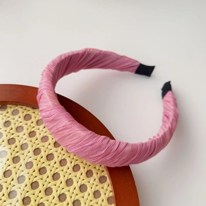 Detailed view of a pink pleated fabric headband displayed on a rustic rattan tray