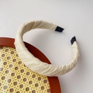 Detail view of cream pleated fabric headband with delicate texture and black end tips