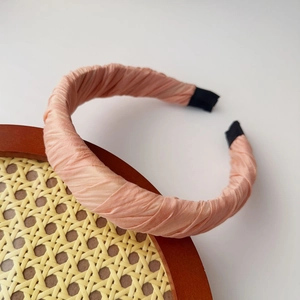Close-up of pink pleated fabric headband with black ends on a rustic woven frame