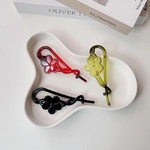 Detailed macro view of three matte flower hair clips in red, green, and black colors