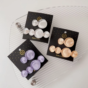 Detailed view of three resin hair clips in purple, ivory, and champagne on a glass tray