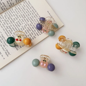 Close-up of four colorful resin cherry hair clips on an open book background
