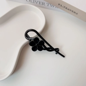 Detail of a minimalist black five-petal flower hair clip on a white ceramic display tray
