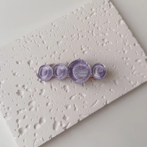 Detailed macro view of purple resin hair clip with wavy circular motifs and golden metal base