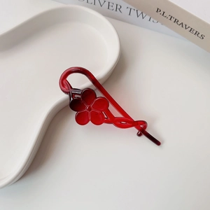Close-up of translucent dark red resin flower banana hair clip on a white ceramic tray