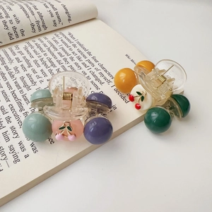 Detail view of two mini cherry hair claws with colorful beads on a book page