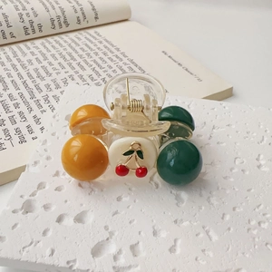 Detail of a mini cherry hair claw with colorful beads on a white textured background