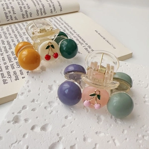 Close-up of small cherry hair clips with colorful beads on a white textured stone