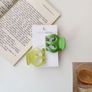 Close-up of two green jelly pumpkin hair claws on a card with a stylish lifestyle background