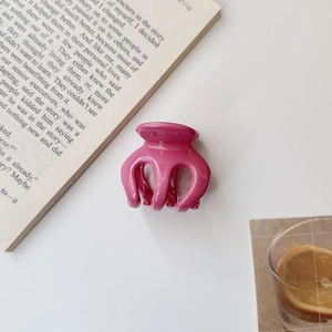 Top view of a bright pink pumpkin claw clip on white surface with artistic book details