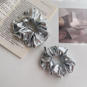Dettaglio di elastici scrunchie metallizzati argento con texture a pieghe su sfondo