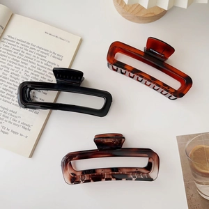 Close-up of large acrylic hair claws in black, amber, and marble on a white surface