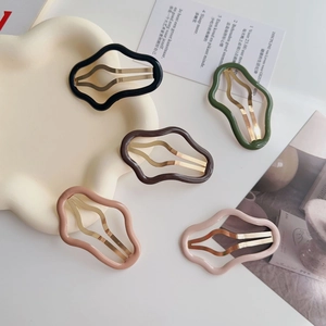 Dettaglio di cinque fermagli per capelli ondulati in vari colori su un vassoio crema