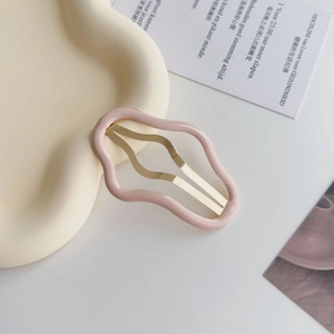 Dettaglio del fermaglio per capelli ondulato rosa opaco con barra dorata su vassoio