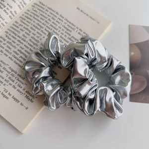 Dettaglio di elastici scrunchie metallizzati argento con pieghe elastiche su sfondo sobrio