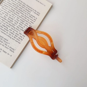 Close-up detail of a matte amber braided twist hair clip on an open book background