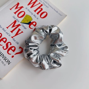 Dettaglio dell'elastico scrunchie argento metallizzato su un libro con trama plissettata