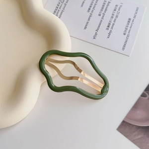 Dettaglio di un fermaglio per capelli verde ondulato con chiusura in metallo dorato
