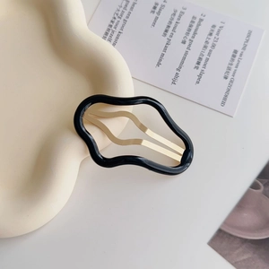 Dettaglio di un fermaglio per capelli nero ondulato con clip in metallo dorato su vassoio