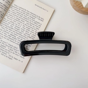Close-up of a large glossy black rectangle hair claw clip on an open book background