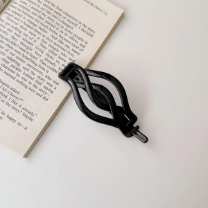 Close-up of a black hollow wave-shaped hair clip placed on an open vintage book
