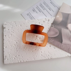 Detail of amber tortoiseshell square hair claw clip on a textured white aesthetic background