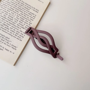 Detail of dark purple matte hair claw with twisted hollow design on an open book