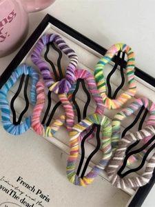Close-up of eight handmade colorful knitted yarn hair clips on a display tray
