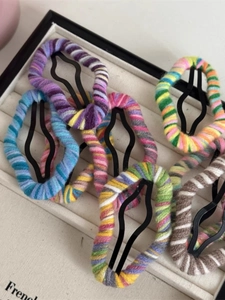 Macro detail of colorful hand-knitted yarn hair clips on a white fabric tray