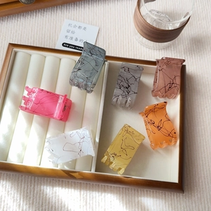 Detail of six matte rectangular hair claws with spider web patterns in a display box