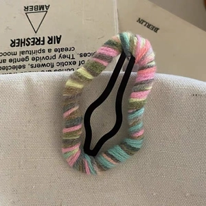 Detailed view of hand-knitted rainbow yarn patterns on a metallic black snap hair clip