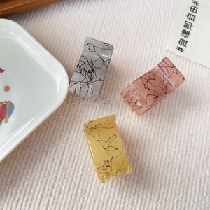 Detail of three marble textured hair claws in grey, pink, and yellow on soft knit fabric