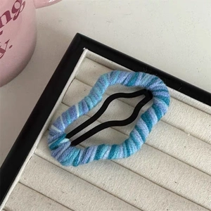 Macro shot of blue gradient yarn-wrapped BB hair clip on a beige velvet jewelry tray