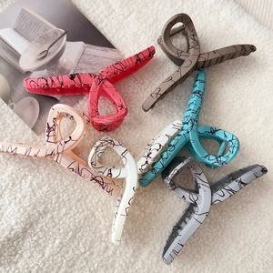Set of six large matte hair claws with modern graffiti patterns on a soft textured background