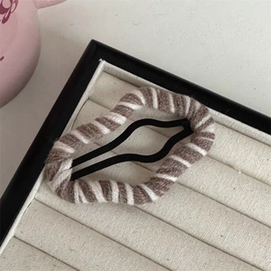 Detail of brown and white striped knit fabric hair clip on a beige jewelry cushion