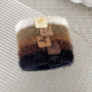 Gros plan de cinq chouchous en peluche aux tons terre avec étiquettes en cuir minimalistes