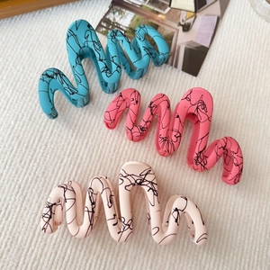 Detailed view of wavy shark hair clips in blue, pink, and beige with ink splatter texture