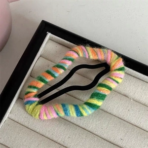 Detailed close-up of a rainbow knitted yarn hair clip on a beige display box