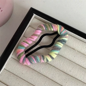 Detail of colorful hand-knitted yarn covering a wavy black metal snap hair clip on velvet