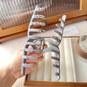 Detail of a large matte white hair claw clip with black ink splatter and strong metal spring