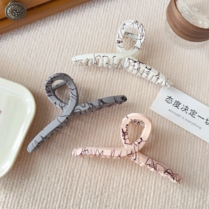 Detailed close-up of large resin hair claws in white, pink, and grey with ink patterns