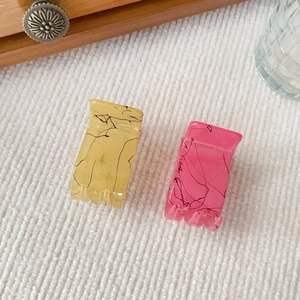 Detail of pink and yellow marble pattern mini hair claws on white soft fabric