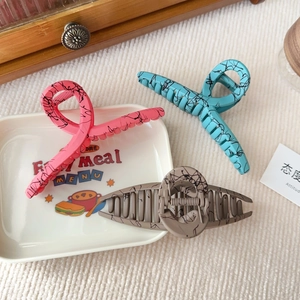 Close-up of matte acrylic claw clips in pink, blue, and grey with marble ink patterns