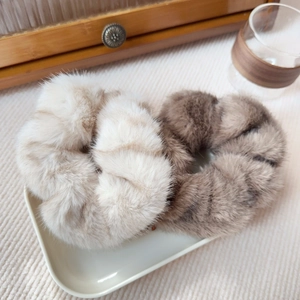 Close-up of beige striped and dark brown faux mink fur scrunchies on a white tray